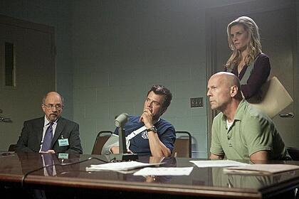 Bruce Willis sentado ao lado de policiais em cena do filme Fogo contra Fogo