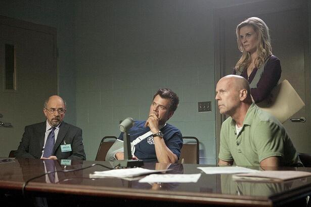 Bruce Willis sentado ao lado de policiais em cena do filme Fogo contra Fogo