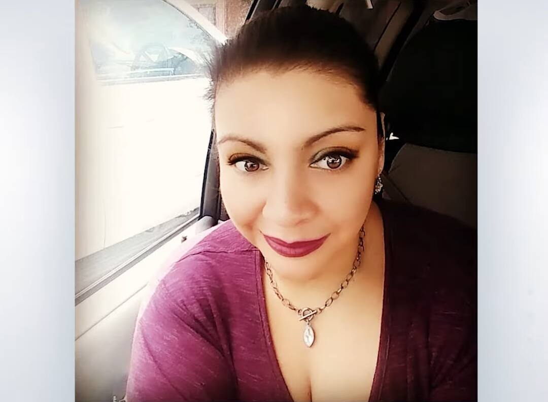 Karina de blusa vinho, sorridente, com batom vermelho em um banco de carro