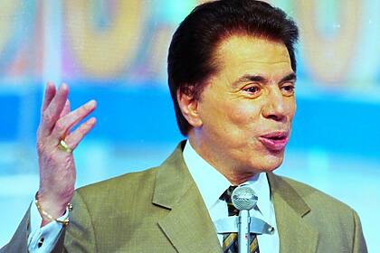 Silvio Santos levanta o braço esquerdo e carrega um microfone no peito