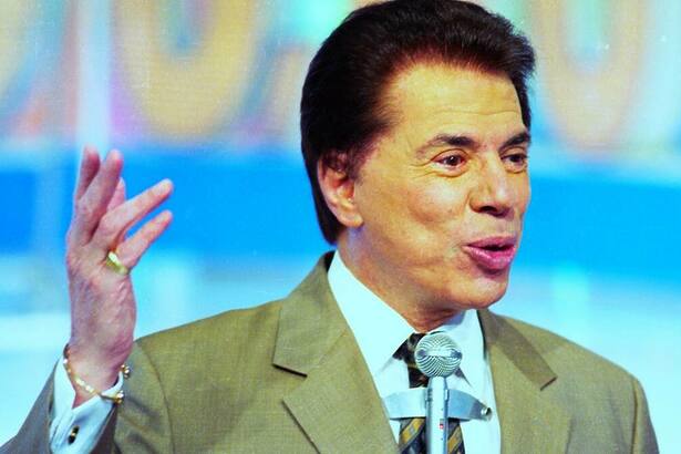 Silvio Santos levanta o braço esquerdo e carrega um microfone no peito