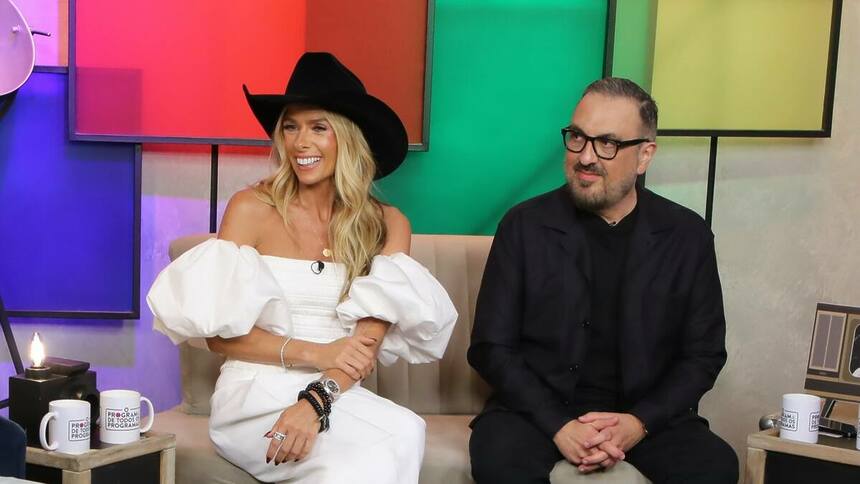 Adriane Galisteu e Rodrigo Carelli sorridentes e sentados no sofá do Programa de Todos os Programas no Portal R7