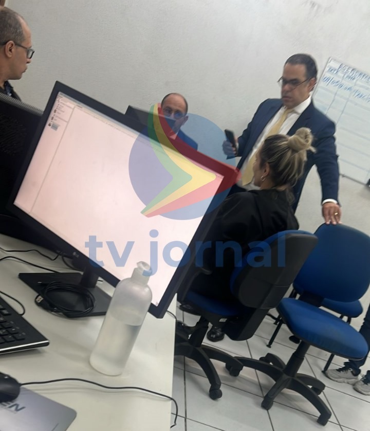 Deolane Bezerra sentada, prestando depoimento na delegacia, em uma foto com marca d'água da TV Jornal 