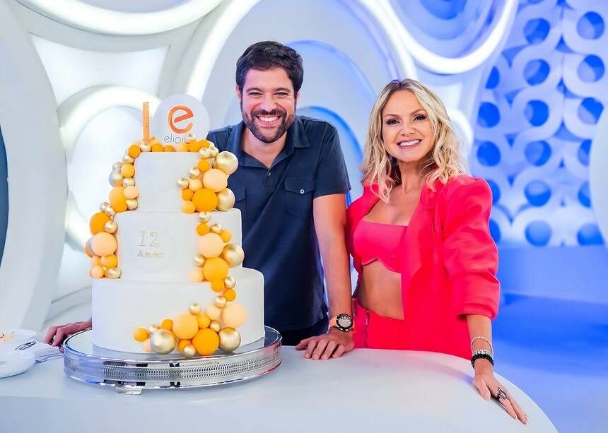 Ariel Jacobowitz ao lado de Eliana no estúdio do SBT. Os dois estão sorridentes ao lado de um bolo