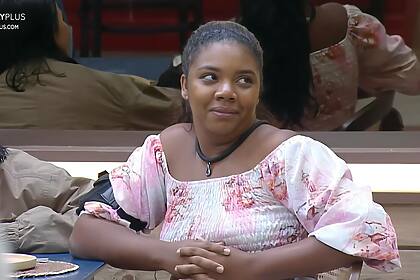 Raquel Brito emocionada, com olhos cheios de lágrimas e sorrindo de canto, sentada na mesa de A Fazenda 16