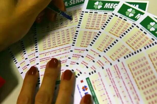Uma mão preenchendo uma cartela de sorteio da Mega-Sena