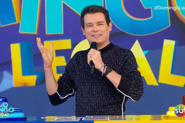 Celso Portiolli no cenário do Domingo Legal. Apresentador veste preto e está sorrindo