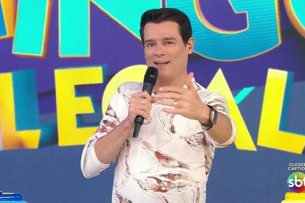 Celso Portiolli apresenta o Domingo Legal segurando microfone preto e com camisa clara estampada