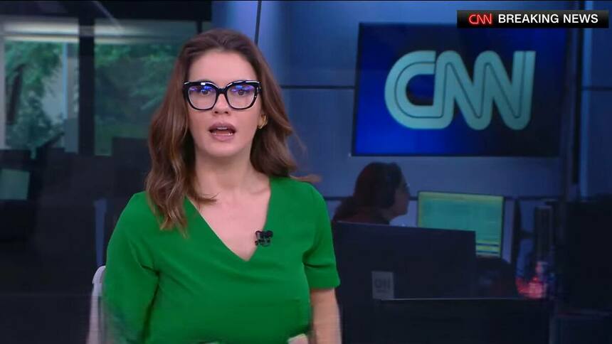 Elisa Veeck de óculos de grau e blusa verde na redação da CNN Brasil