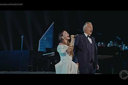 Mulher vestida de branco canta ao lado do Tenor Andrea Bocelli