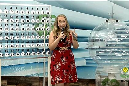 Apresentadora do Alagoas dá Sorte de vestido vermelho em frente ao globo e das bolas do sorteio deste domingo, 26/01/2025