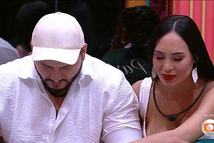 Marcelo com a cabeça baixa de boné branco e Arleane olhando para o chão no BBB 25