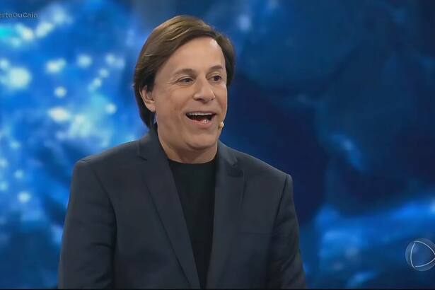 Tom Cavalcante sorrindo no palco do Acerte ou Caia com o cenário em azul