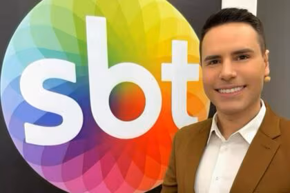Logo do SBT no quadro do camarim onde Luiz Bacci aparece de terno marrom e microfonado