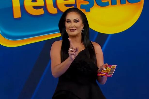 Helen Ganzaolli segura bilhete da Tele Sena de Carnaval 2025. Ela está de vestido preto no cenário do SBT