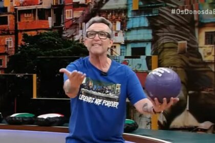 Craque Neto surtado e com uma bola na mão no cenário de Os Donos da Bola