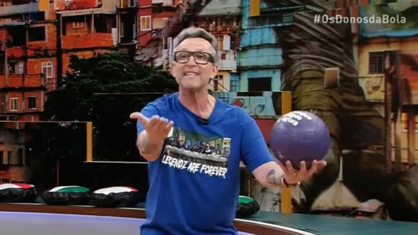 Craque Neto surtado e com uma bola na mão no cenário de Os Donos da Bola