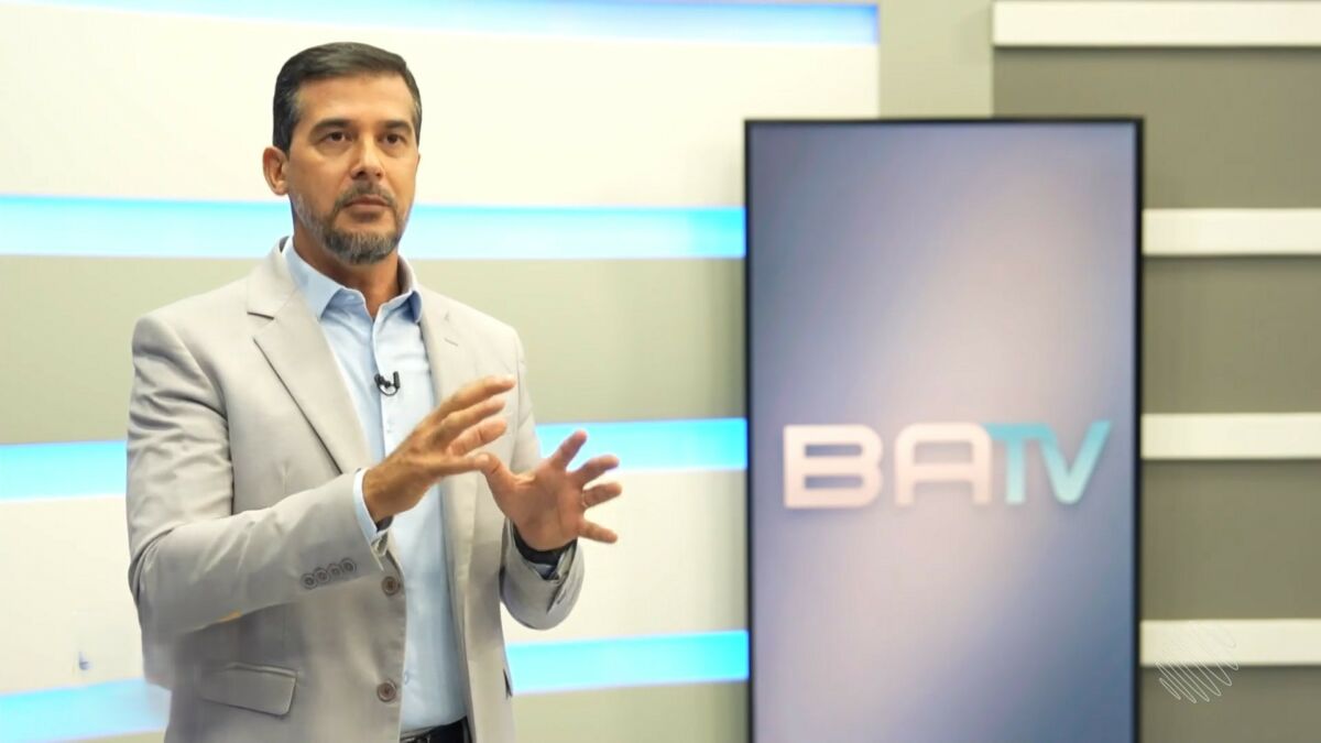 Fernando Sodake ao lado de uma das telas verticais do cenário com o logo do BATV