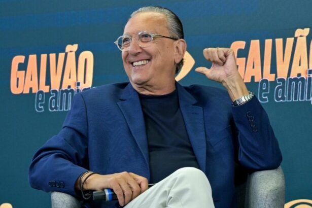 Galvão Bueno sorridente, sentado em uma poltrona, em trecho da coletiva