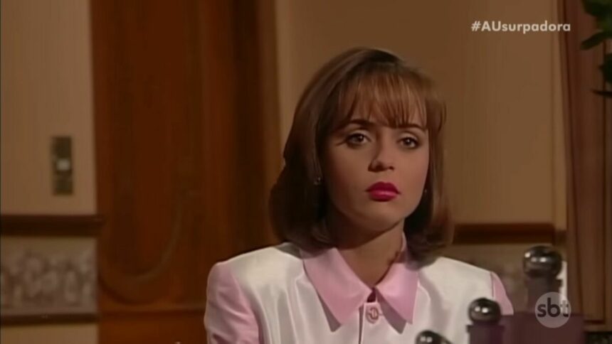 Paulina com roupa rosa em cena da novela A Usurpadora. Ela está olhando para um espelho de maquiagem