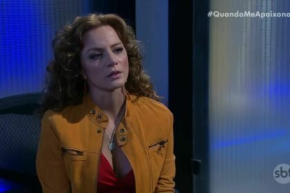 Silvia Navarro como Renata, de Quando Me Apaixono. Ela está de jaqueta marrom sentada em uma cadeira de escritório