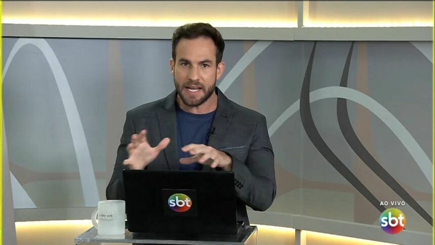 Daniel Adjuto com as mãos levantadas sobre o notebook no cenário do SBT Brasília