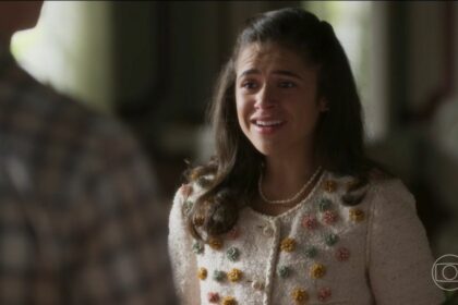 Bia com roupa branca florida, olha para Beto e sorrir em cena da novela Garota do Momento