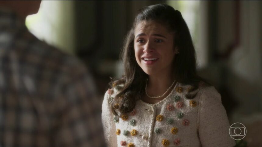 Bia com roupa branca florida, olha para Beto e sorrir em cena da novela Garota do Momento
