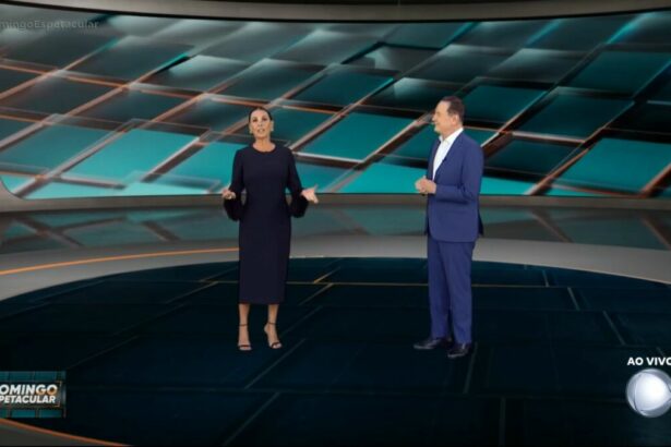 Carolina Ferraz, de vestido preto e com as mãos abertas ao lado de Roberto Cabrini na apresentação do Domingo Espetacular