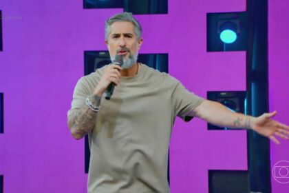 Marcos Mion com os braços abertos no palco do Caldeirão falando de cantores sertanejos