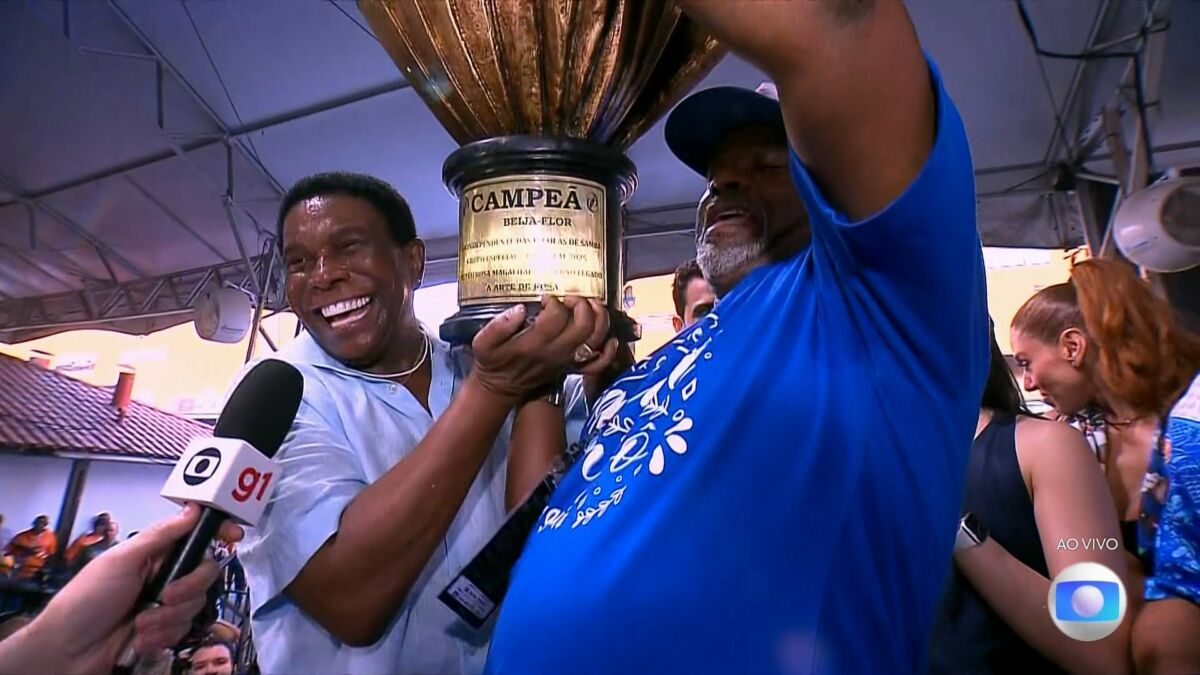 Neguinho, sorrindo, levanta o troféu da campeã