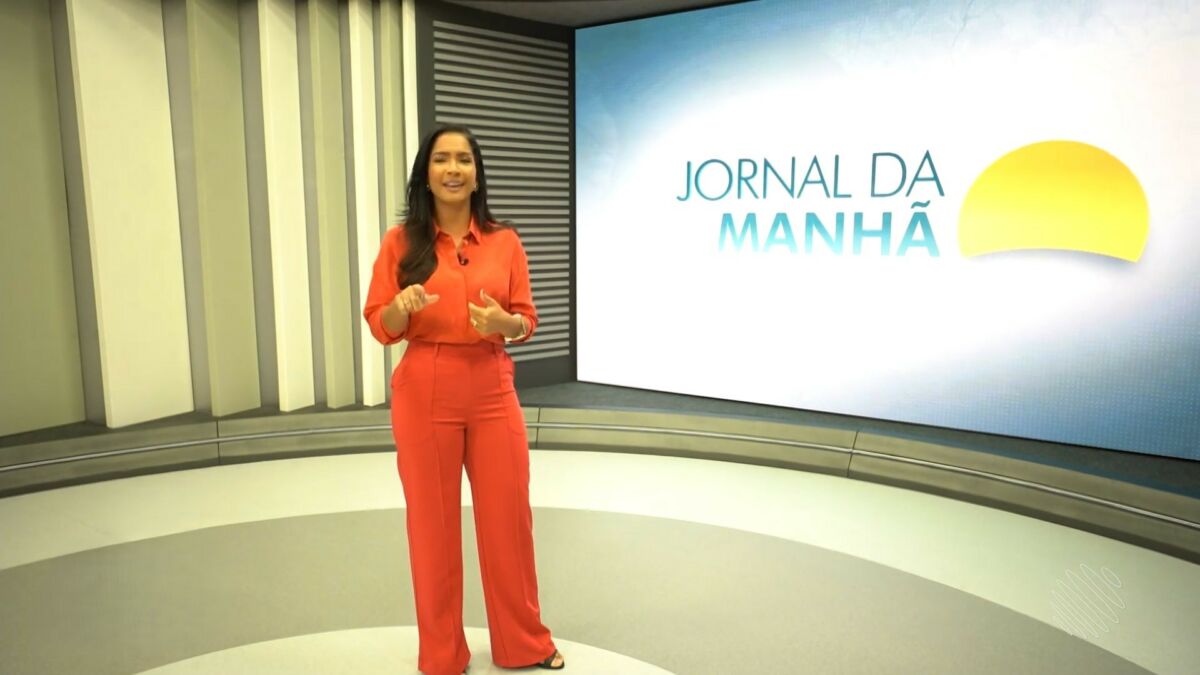 Camila Oliveira, de vestido laranja, em frente ao telão do Jornal da Manhã