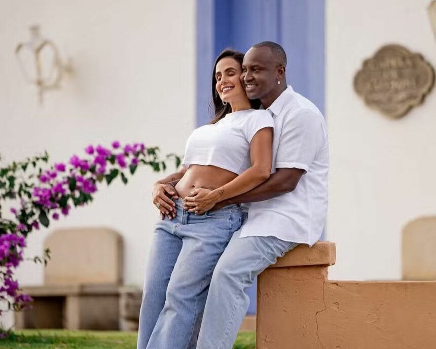 Thiaguinho acaricia barriga de grávida de Caro Peixinho, os dois estão sorridentes e um jardim