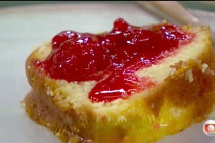 Pedaço de bolo de laranja molhadinho com uma geleia de cor vermelha por cima no prato do mais você
