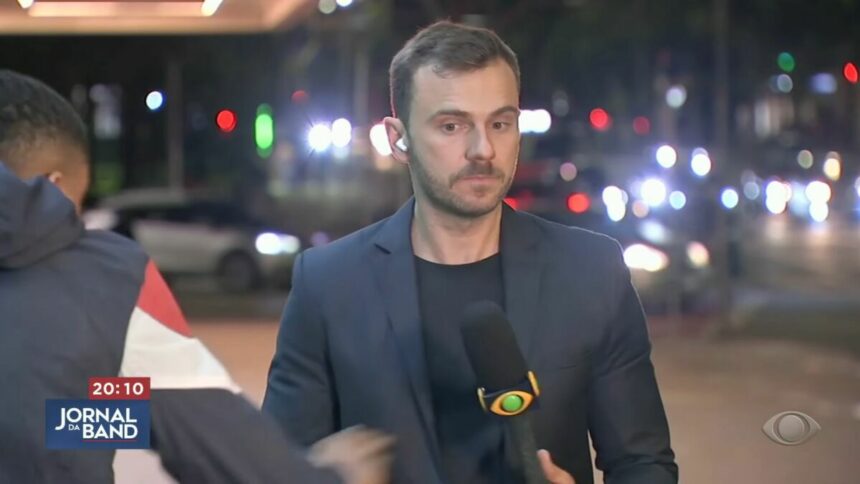 Igor Calian, com o microfone da Band nas mãos, com o ciclista passando e tentando puxar o celular