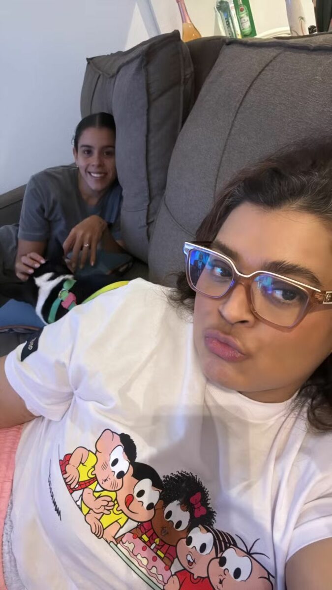 Preta Gil deitada no sofá de casa, ao lado de uma amiga, após alta do hospital 