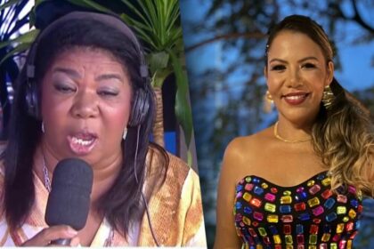 Elisangela com o microfone e fone de ouvido na porta da RECORD Bahia. Ela está com a boca aberta concedendo entrevista. Mani Rego veste um cropped colorido de pedras brilhantes. Ela está no entardecer e sorrindo.