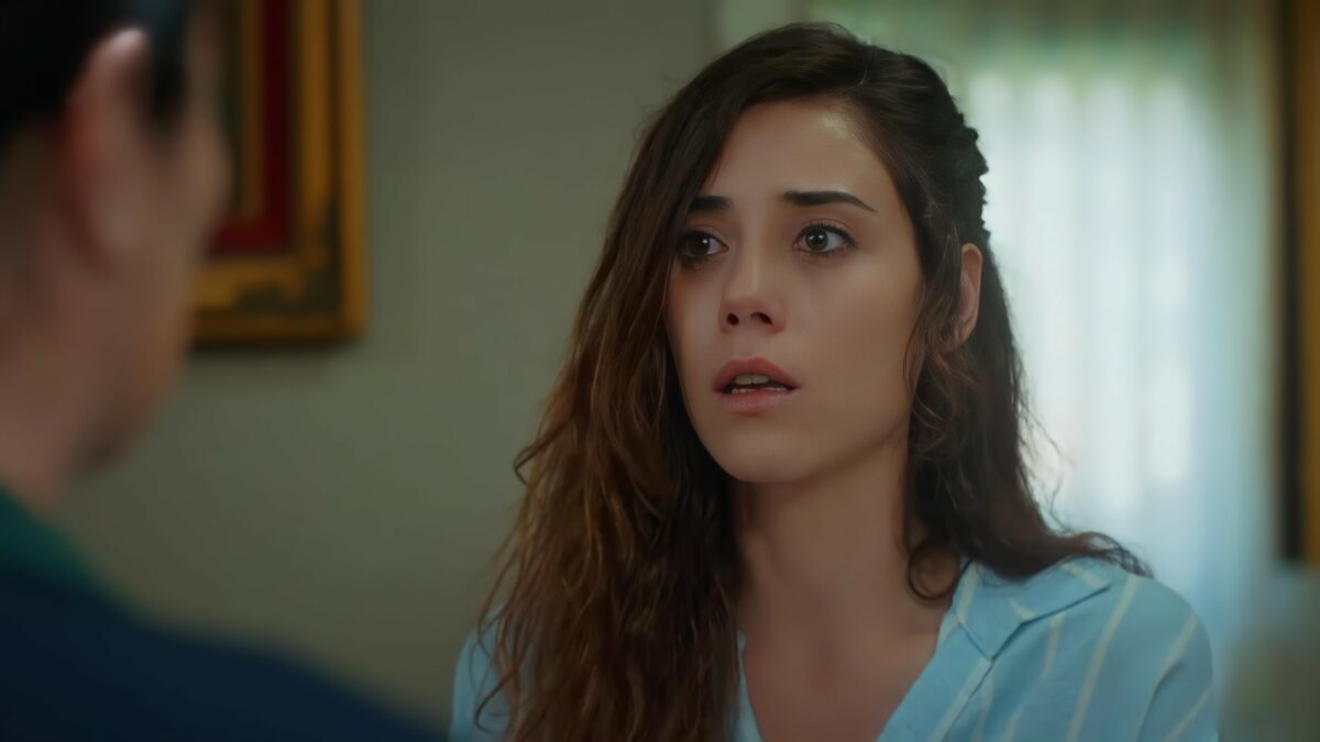 Cansu Dere na sala de de uma casa, em cena dramática da novela turca Mãe. A personagem olha para sua mãe com olhar assustado