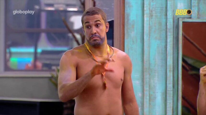 Maike todo pintado de fumaça colorida do Sincerão, no gramado da casa do BBB 25 com a mão levantada