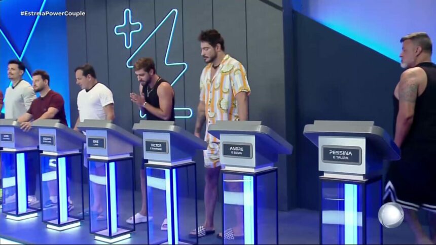 Homens na sala de apostas do Power Couple Brasil 7. Eles estão posicionados atrás de púlpitos com seus respectivos nomes