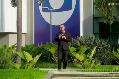 repórter Léo Sant’Anna gravando reportagem do SBT Brasil no jardim dos Estúdios Globo, em frente ao logo da TV Globo em azul