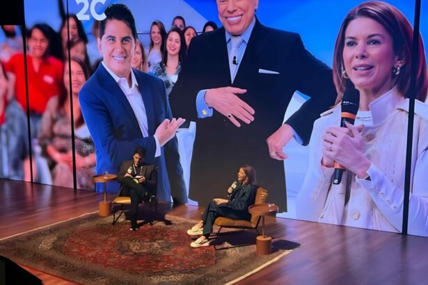 Cesar Filho sentado ao lado de Daniela Beyruti. Eles estão em frente a um telão gigante que trás imagens dos dois e de Silvio Santos no Rio2C