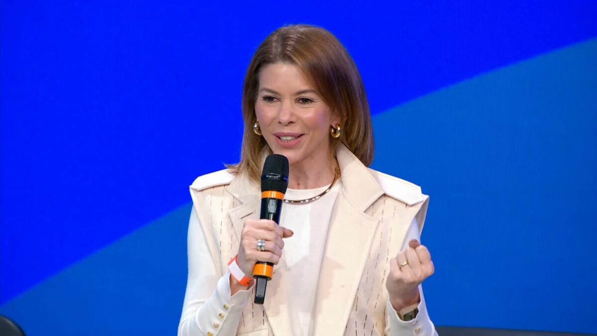 Daniela Beyruti, CEO do SBT, segura microfone da emissora em frente a um grande telão com fundo azul
