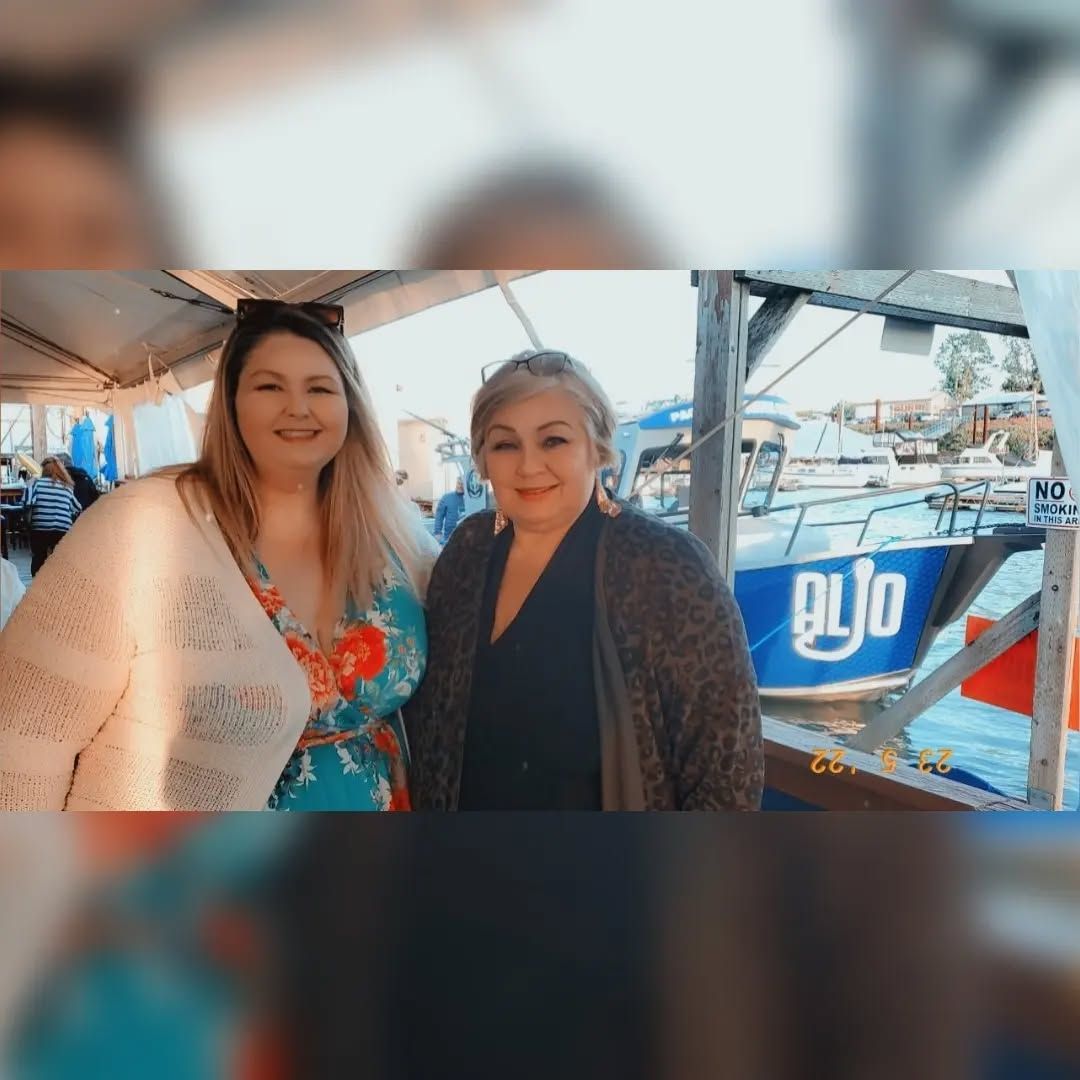 Maja ao lado de uma mulher. Ao fundo barcos em uma praia