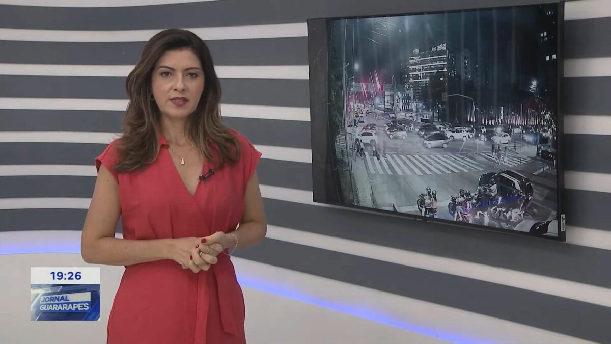 Meiry Lanunce de vestido vermelho em frente a uma tela no cenário do Jornal Guararapes