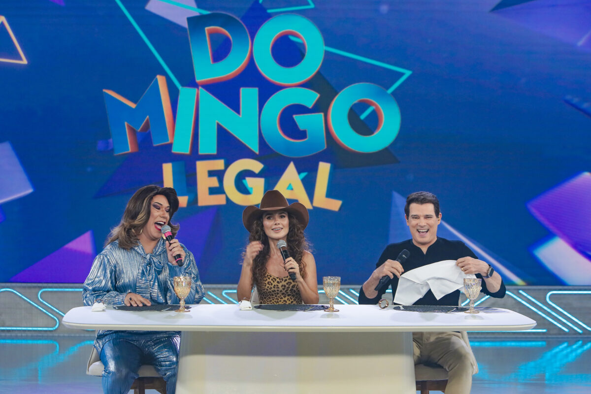 Narcisa, Paula Fernandes e Celso Portiolli sentados em uma bancada no centro do cenário do domingo Legal 