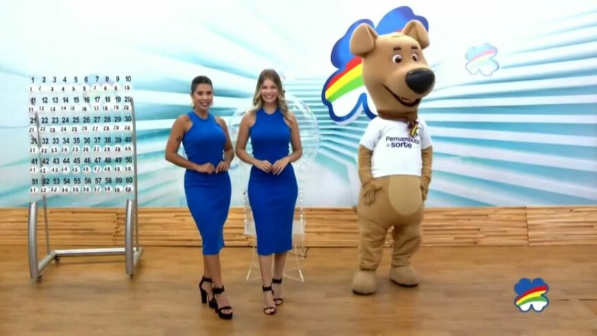 Assistentes de palco vestem azul, posicionadas ao lado do painel com as bolas e o mascote do sorteio do Pernambuco dá Sorte