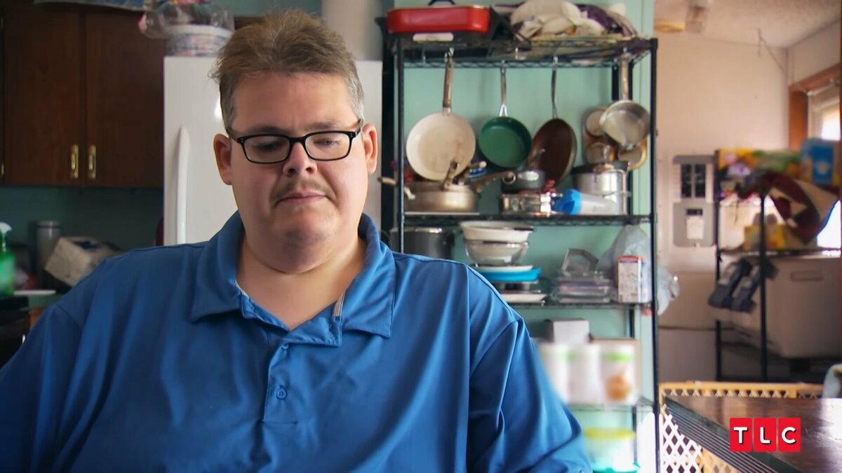 Aaron de camisa azul em uma cozinha