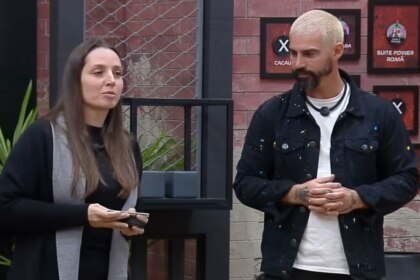Carol e Radamés em frente ao quadro da divisão de quartos no Power Couple Brasil 7