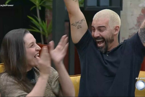 Carol e Radamés celebram vitória na Prova dos casais. Radamés levanta os braços, sentado no sofá, enquanto Carol bate palmas